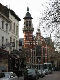 Scène urbaine à Jette avec technicien en débouchage devant une maison typique et rues pavées de la ville.