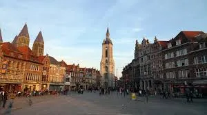 Rue animée de Tournai avec véhicules de débouchage en action sur fond de la Cathédrale Notre-Dame renommée.